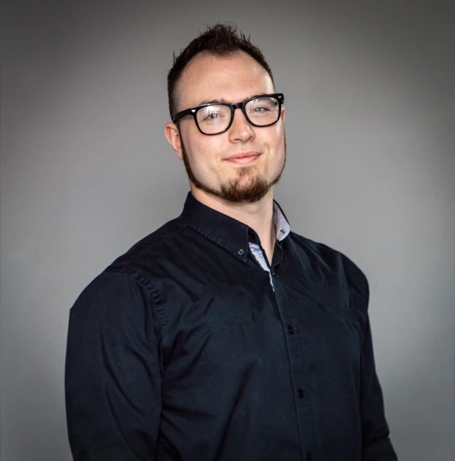 Isaac Birchall in a dark shirt and glasses, smiling